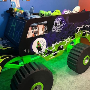 Könnte beinhalten: Ein bettförmiger Monster Truck, bemalt in Schwarz, Grün und Lila. Das Bett hat eine Totenkopf-Grafik und eine Geisterhaus-Szene. Die Räder sind groß und schwarz mit grünen Akzenten. Das Bett ist mit Stofftieren gefüllt.