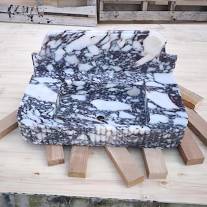 May include: A rectangular marble sink with a basin and a backsplash. The sink features a white and dark purple veined pattern. The sink is supported by wooden blocks. The sink is designed for bathroom use.