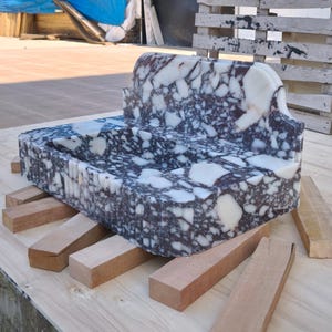 May include: A rectangular marble sink with a unique design, featuring a mix of white and dark gray patterns. The sink is supported by several wooden blocks, showcasing a natural stone aesthetic. The sink's dimensions are not visible.