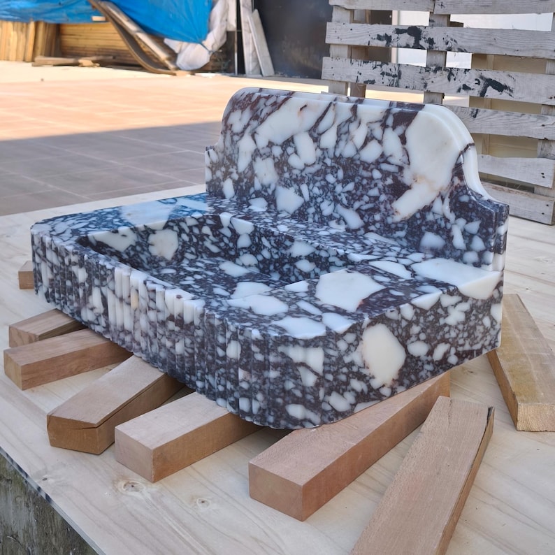 May include: A rectangular marble sink with a unique design, featuring a mix of white and dark gray patterns. The sink is supported by several wooden blocks, showcasing a natural stone aesthetic. The sink's dimensions are not visible.