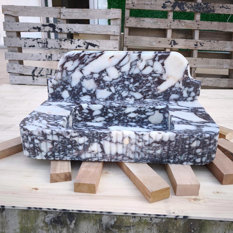 May include: A marble bench with a unique design. The bench features a white and dark gray patterned surface. The bench is supported by several wooden beams. The bench has a rectangular shape with a curved backrest.