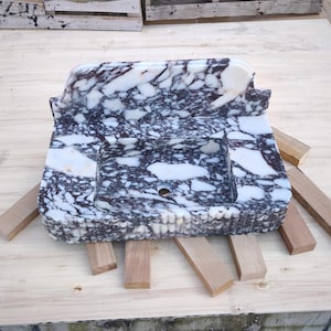 May include: A rectangular marble sink with a white and dark purple patterned design. The sink has a basin and a raised back. It is resting on wooden supports.