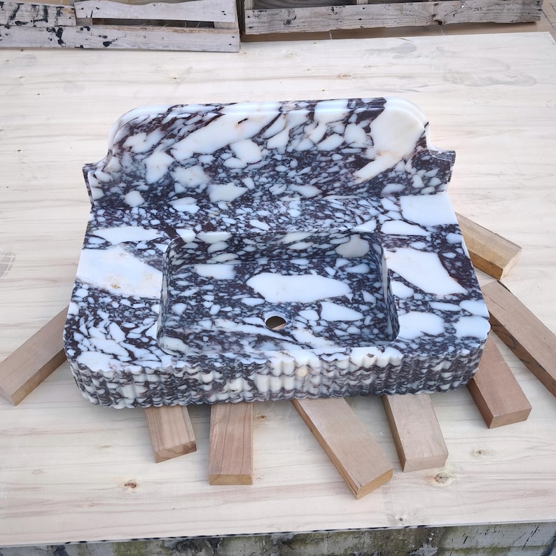 May include: A rectangular marble sink with a white and dark purple patterned design. The sink has a basin and a raised back. It is resting on wooden supports.