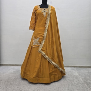 May include: Mustard yellow formal dress with intricate embroidery and gold trim. The dress features a long skirt, three-quarter sleeves, and a matching shawl. The bodice and sleeves have delicate embellishments, adding a touch of elegance to the ensemble.