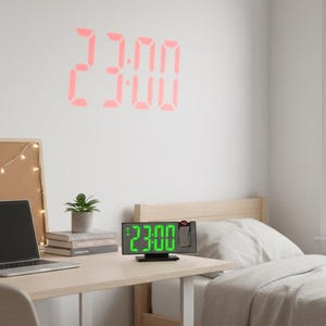 以下が含まれることがあります： 緑色のLEDディスプレイで23:00を表示するデジタル時計。時間は壁に赤色で投影されます。時計は、ラップトップ、コルクボード、小さな植物のある机の上にあります。部屋にはベッドと窓があります。