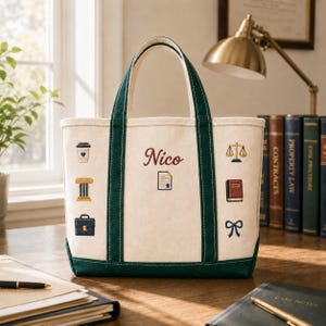 Puede incluir: Un bolso de lona color crema con bordes y asas de color verde oscuro. El bolso presenta iconos bordados que incluyen una taza de café, una columna, un maletín, una balanza de justicia, un libro y un lazo. El nombre Nico está bordado en rojo.