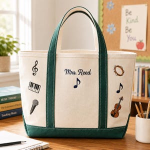 May include: Cream-colored tote bag with dark green accents and handles. The bag features musical instrument graphics and the name "Mrs. Reed" in navy blue. A treble clef, piano keys, microphone, tambourine, musical notes, and a violin are displayed.