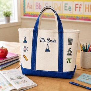 May include: Cream-colored canvas tote bag with blue accents, handles, and base. The bag features science-themed graphics and the name "Ms. Brooks." Additional details include a calculator, microscope, and the pi symbol.