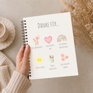 Può includere: Un quaderno a spirale con la scritta "DANKE FÜR..." in alto. Sotto, illustrazioni ad acquerello di un orsacchiotto, un cuore, un arcobaleno, un sole, matite e fiori, ognuno con una parola tedesca.