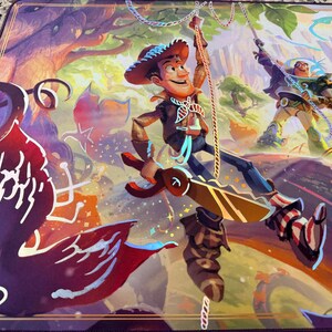 May include: A vibrant playmat featuring a colorful illustration of Woody and Buzz Lightyear from Toy Story. Woody is sliding down a rope, while Buzz is swinging on a rope in a forest setting. The mat has a purple border and a detailed, artistic design.