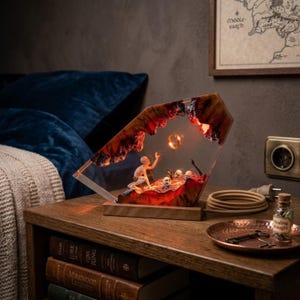 May include: A decorative lamp with a fantasy scene inside a clear resin structure. The lamp features a figure reaching for a glowing ring, with a warm, reddish-orange internal glow. It sits on a wooden base, creating a unique, themed ambiance.