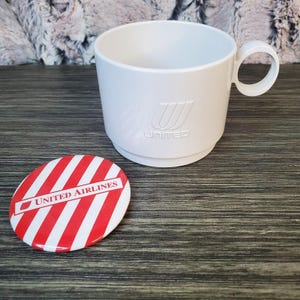 Peut inclure: Une tasse en plastique blanc avec une poignée et le logo "United" en relief. À côté, un dessous de verre rond à rayures rouges et blanches avec "United Airlines" imprimé. La tasse et le dessous de verre sont probablement des souvenirs d'avion vintage.