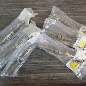 May include: Five brass-toned metal cabinet pulls, each individually sealed in clear plastic packaging. The hardware features a cylindrical design with decorative rings and includes small mounting screws visible inside the bags.