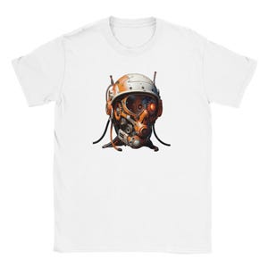 Puede incluir: Camiseta blanca con una ilustración detallada de un casco futurista. El diseño presenta elementos naranjas, blancos y gris metálico, incluyendo engranajes, tubos y un ojo rojo brillante, creando una estética de ciencia ficción.
