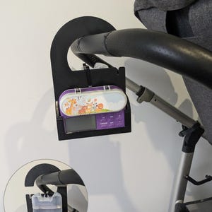 May include: A black stroller organizer with a purple and white case featuring animal illustrations. The organizer is attached to a stroller handle. A water bottle holder is also attached to the stroller handle.