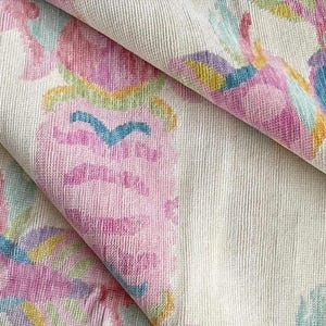 Può includere: Primo piano di un tessuto piegato con un motivo floreale colorato. Il design presenta tonalità rosa, blu, gialle e verdi su uno sfondo color crema. Il tessuto ha un aspetto strutturato, con fili intrecciati visibili.