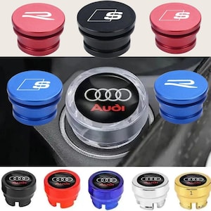 May include: A collection of car accessories, including red, black, blue, and gold ignition button covers. The covers feature the Audi logo and various stylized "S" and "R" designs in white. The accessories are shown on a car's dashboard.