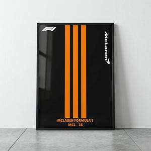 May include: Framed poster with a black background and three vertical orange stripes. The McLaren Formula 1 poster features the McLaren logo and F1 logo in white. The text "MCLAREN FORMULA 1 MCL-36" is at the bottom. The poster is in a black frame.