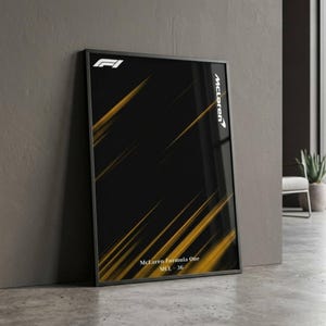 May include: Framed McLaren Formula One poster. The poster has a black background with diagonal gold streaks. The McLaren logo and Formula One logo are in white. The text "McLaren Formula One MCL-36" is at the bottom of the poster.