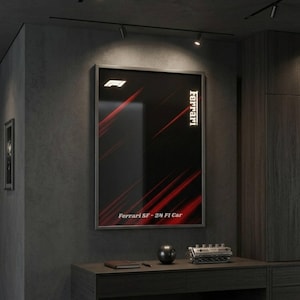 Puede incluir: Un póster enmarcado con el logotipo de Ferrari y el texto "Ferrari SF-24 FI Car" sobre un fondo negro con rayas diagonales rojas. El póster está colgado en una pared gris oscura sobre una mesa de madera oscura.