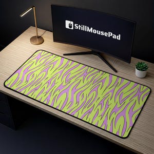 May include: A rectangular mousepad featuring a bold design of lime green and lavender zebra stripes. The mousepad has a black border and is positioned on a wooden desk. A computer monitor with the text "StillMousePad" is visible in the background.