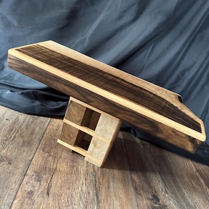 Peut inclure: Un présentoir rectangulaire en bois doté d'une surface supérieure brun foncé au grain horizontal et de bords en bois clair. La base est constituée d'un bloc de bois clair avec un motif en grille et des sections carrées ouvertes visibles.