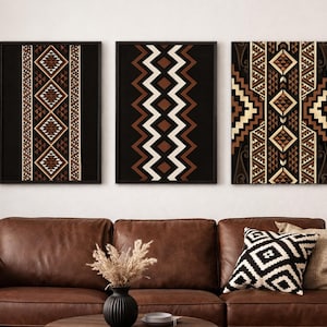 Pode incluir: Três obras de arte emolduradas com padrões geométricos em tons de castanho, bege e branco sobre um fundo preto. As obras de arte são exibidas acima de um sofá de couro castanho com almofadas decorativas.