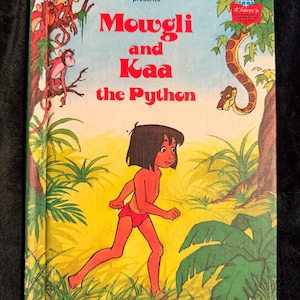 May include: A vintage hardcover book titled "Mowgli and Kaa the Python" by Walt Disney Productions. The cover features a colorful illustration of Mowgli running, with monkeys, a snake, and jungle foliage. The book has a retro aesthetic.