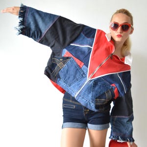 May include: A patchwork jacket featuring panels of blue denim, black fabric, and bright red accents with a front zip, white collar, and frayed sleeve cuffs, paired with dark blue denim shorts and red high-heeled shoes with red sunglasses.