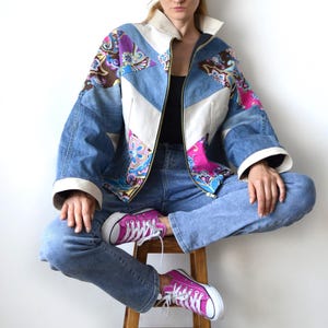 May include: A zip-up jacket featuring a patchwork design of blue denim, cream-coloured fabric, and panels with a vibrant pink, purple, and blue paisley pattern. The jacket has a high collar, long sleeves with wide cuffs, and a front zipper closure.