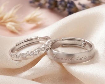 Könnte beinhalten: Zwei silberne Ringe auf einer Satin-Oberfläche. Ein Ring hat eine Reihe kleiner, klarer Steine. Der andere Ring trägt den eingravierten Text "You are the best to me."