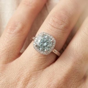 Könnte beinhalten: Ein silberner Ring mit einem großen, hellblauen, kissenförmigen Edelstein, umgeben von einem Halo aus kleineren, klaren Steinen. Der Ring sitzt auf einem zarten Band und zeigt ein klassisches und elegantes Design. Der Ring ist ein Schmuckstück.