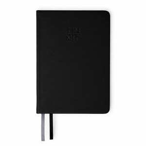 Peut inclure: Un carnet noir à la couverture lisse et mate, orné d'un logo en relief au centre portant l'inscription "ΓΜ|ΜΓ". Le carnet comporte deux marque-pages en ruban dépassant du bord inférieur, l'un gris clair et l'autre noir uni.