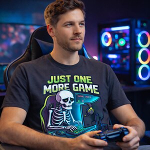 A man wearing a t-shirt with a graphic of a skeleton playing a video game, sitting in a gaming chair in front of a computer monitor.