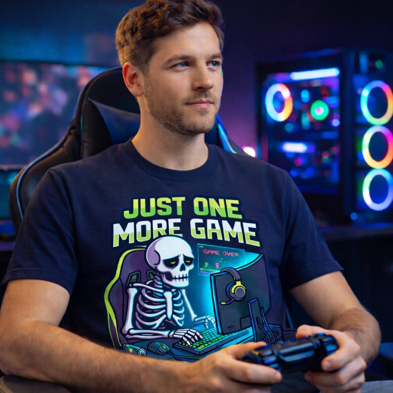 A man wearing a t-shirt with a graphic of a skeleton playing a video game, sitting in a gaming chair in front of a computer monitor.