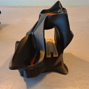 May include: A black, abstract sculpture with a cave-like opening. The interior features a section of tan train tracks. The sculpture has a glossy finish with hints of orange and red.