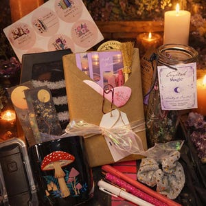 May include: A collection of items including a black mug with a red mushroom illustration, a brown paper-wrapped package, a glass jar labelled Crystal Magic, a sheet of bookplate stickers, two pens, a hair scrunchie, and a small decorative broom.