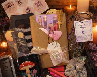 Op de afbeelding: Een assortiment items, waaronder een zwarte mok met een paddestoelontwerp, pennen, stickers, een pot met het label "Crystal Magic" en kaarsen. De items zijn gerangschikt op een houten oppervlak met een zachte, warme gloed.
