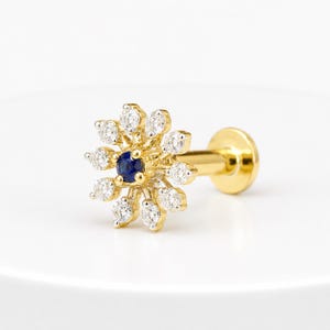 May include: A gold labret stud earring featuring a central round blue sapphire surrounded by a halo of twelve clear, round-cut white stones arranged in a floral pattern. The post is gold with a flat circular disc backing for secure placement.