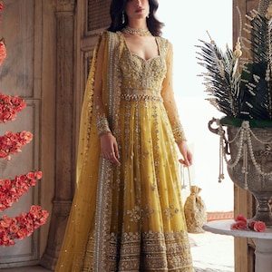May include: A mustard yellow floor-length lehenga choli featuring intricate silver embroidery, beadwork, and sequins. The ensemble includes a long-sleeved bodice, a voluminous skirt with a wide embellished hem, and a matching sheer dupatta.