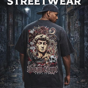 Könnte beinhalten: Dunkelgraues T-Shirt mit einer Grafik, die eine klassische Büste, Rosen, eine Schlange und einen Totenkopf zeigt. Das Shirt trägt den Text "Urban Crypt Project STREETWEAR" in einer gotischen Schriftart. Die Person trägt eine schwarze Kappe.