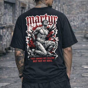 Könnte beinhalten: Schwarzes T-Shirt mit einem Grafikdruck auf der Rückseite, der eine gefesselte Figur zeigt, das Wort "MARTYR" in einer stilisierten Schriftart und den Text "THEY BROKE MY CHAINS BUT NOT MY SOUL". Das Design enthält rote Akzente und Kettendetails.