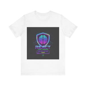 Op de afbeelding: Wit T-shirt met een kleurrijke afbeelding. De afbeelding bevat een hersenontwerp in een schild, het woord "REACT" en de tekst "TEAM LEADERS DEVELOPER TEAM". Het ontwerp heeft een futuristische, digitale uitstraling.