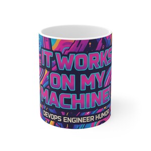 May include: White ceramic mug with a colourful design. The mug features the text "IT WORKS ON MY MACHINE!" in a vibrant pink and blue font, with "DEVOPS ENGINEER HUMOR" below.