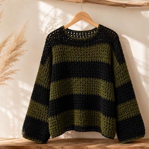 Puede incluir: Un su&eacute;ter de manga larga con un patr&oacute;n de rayas horizontales en colores negro y verde oliva alternados. La prenda est&aacute; confeccionada con un punto de ganchillo abierto, cuello redondo y un corte holgado, colgado de una percha de madera.