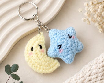 Puede incluir: Un llavero de ganchillo con una media luna de color amarillo pálido y una estrella de color azul claro, ambos con ojos cerrados bordados y mejillas rosadas. Las dos figuras de peluche están unidas a una anilla de metal plateado por cadenas.
