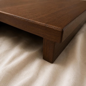 May include: A dark brown wooden tray with a raised edge and a single supporting leg. The tray has a smooth, polished surface and is likely used for serving or display purposes. The wood grain is visible.