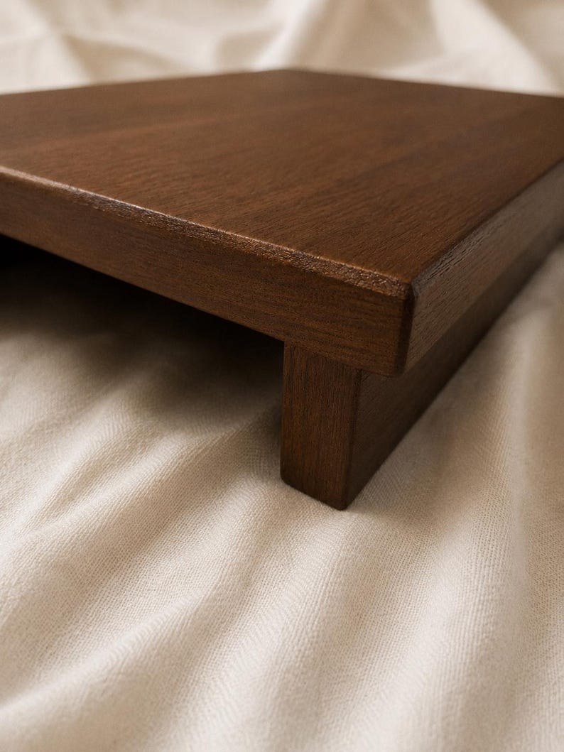May include: A dark brown wooden tray with a raised edge and a single supporting leg. The tray has a smooth, polished surface and is likely used for serving or display purposes. The wood grain is visible.