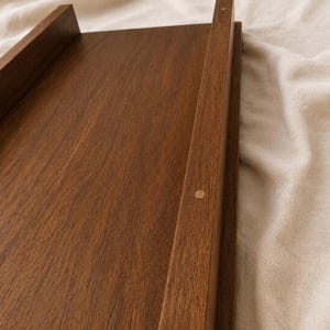 May include: A rectangular wooden tray with raised sides and a rich brown finish. The tray has a simple, minimalist design, with clean lines and a smooth surface. The wood grain is visible, adding to the natural aesthetic.