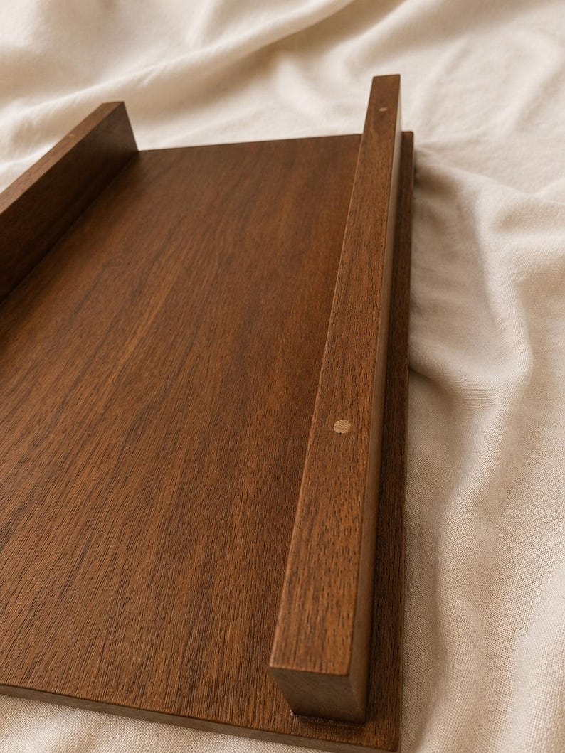 May include: A rectangular wooden tray with raised sides and a rich brown finish. The tray has a simple, minimalist design, with clean lines and a smooth surface. The wood grain is visible, adding to the natural aesthetic.